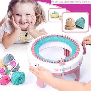 Puede incluir: Máquina de tejer Sentro blanca y rosa con un área de tejido azul y rosa. La imagen también muestra a una niña sonriendo, ovillos de lana y gorros de punto. El texto "DY sweater, scarf, hat knitting machine" es visible.