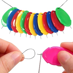 May include: A collection of colorful needle threaders in various colors, including green, blue, red, yellow, and pink. Each threader has a small metal wire loop for easy threading. The image also shows a person using a pink threader.