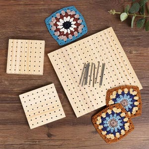 May include: Wooden square and rectangular peg boards with evenly spaced holes, alongside crochet squares in blue, brown, and white. Several metal pins are also present, suggesting a crafting or textile project.