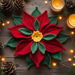 May include: A handmade crochet poinsettia flower with red petals, green leaves, and a yellow center. The flower is placed on a wooden surface, surrounded by pine cones, candles, and string lights, creating a festive holiday scene.