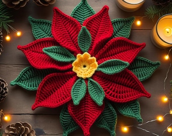 May include: A handmade crochet poinsettia flower with red petals, green leaves, and a yellow center. The flower is placed on a wooden surface, surrounded by pine cones, candles, and string lights, creating a festive holiday scene.