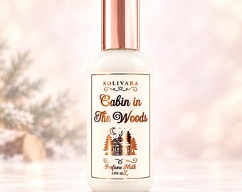 May include: A white opaque bottle with a metallic rose gold cap, containing 100 mL of perfume milk. The label features the text 'SOLIVARA', 'Cabin in The Woods', and 'Perfume Milk' in rose gold, with a graphic of a cabin, trees, and a moon.