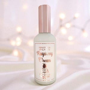 Pode incluir: Uma garrafa de vidro verde claro com tampa e rótulo em ouro rosa. O rótulo diz "SOLIVIA Raspberry Cream" com um gráfico de sobremesa. O fundo é branco macio e desfocado com luzes bokeh.