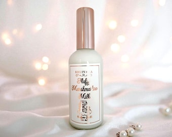 May include: A white perfume bottle with a rose gold cap and label. The label reads "Fluffy Marshmallow Milk" in a decorative font. The bottle is on a white satin surface with a string of pearls.