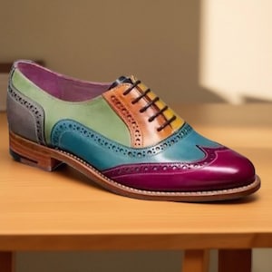 Puede incluir: Un zapato oxford de cuero multicolor con diseño wingtip y perforaciones brogue decorativas. El zapato presenta paneles en magenta, verde azulado, verde, amarillo, naranja y gris, con cordones marrón oscuro y un tacón de madera.