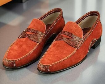 Könnte beinhalten: Ein Paar Loafer aus orangefarbenem Wildleder mit einem dunkelbraunen Riemen aus Leder in Krokodillederoptik über dem Vorderblatt, passenden Lederbesätzen an Ferse und Spitze, hellen Kontrastnähten und einem niedrigen schwarzen Absatz.
