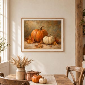 Pu&ograve; includere: Una stampa artistica incorniciata che raffigura una grande zucca arancione e una zucca bianca pi&ugrave; piccola circondate da foglie autunnali cadute. L'opera presenta uno stile pittorico e materico con toni caldi, racchiusa in una cornice in legno chiaro.