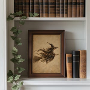 May include: A framed rectangular wall art print featuring a sepia-toned illustration of a witch wearing a pointed hat and tattered robes while flying on a broomstick. The artwork is displayed in a dark brown wooden frame with a simple border.