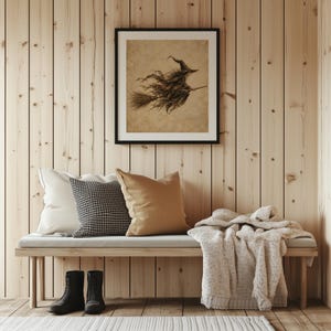 May include: A framed square wall art print featuring a sepia-toned illustration of a witch flying on a broomstick. The artwork is displayed above a wooden bench with a white pillow, a black and white houndstooth pillow, and a tan pillow.