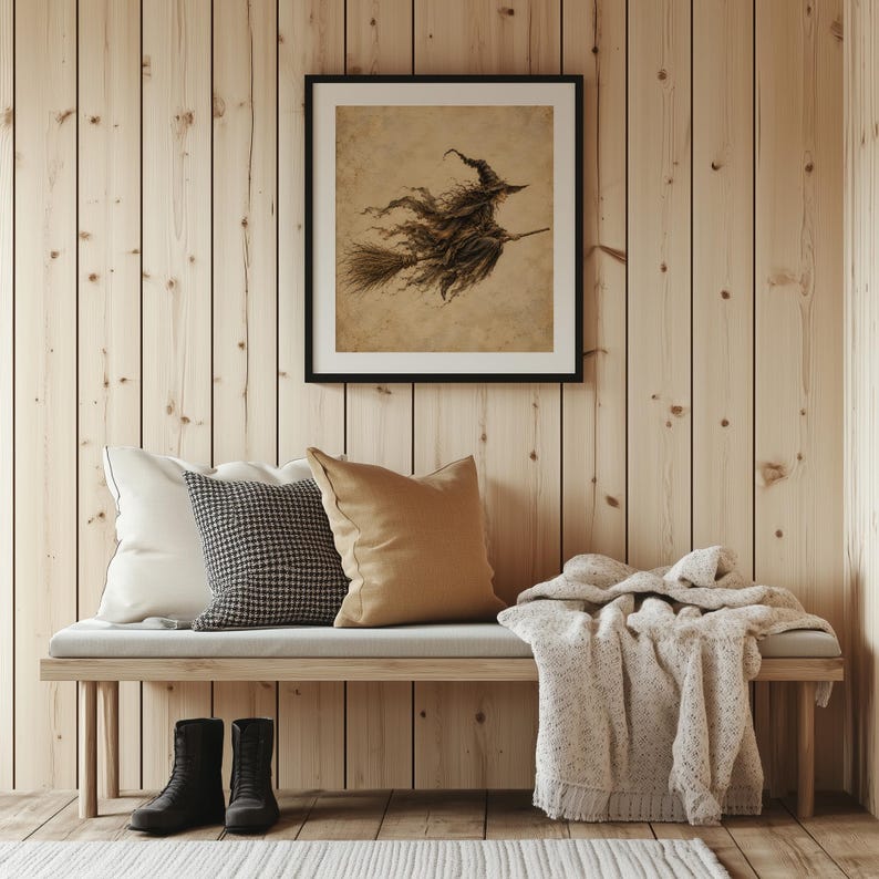 May include: A framed square wall art print featuring a sepia-toned illustration of a witch flying on a broomstick. The artwork is displayed above a wooden bench with a white pillow, a black and white houndstooth pillow, and a tan pillow.