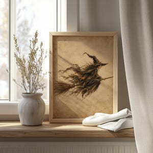 May include: A framed wall art print featuring a sepia-toned illustration of a witch with a pointed hat flying on a broomstick. The artwork is displayed in a light-colored wooden frame, showcasing a weathered, parchment-like background texture.