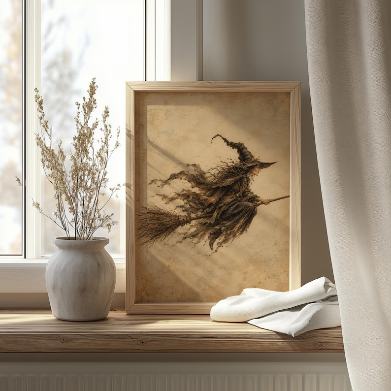 May include: A framed wall art print featuring a sepia-toned illustration of a witch with a pointed hat flying on a broomstick. The artwork is displayed in a light-colored wooden frame, showcasing a weathered, parchment-like background texture.