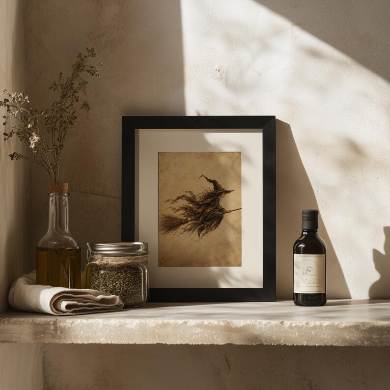 May include: A framed art print featuring a dark, sepia-toned illustration of a witch flying on a broomstick. The print is displayed in a black frame alongside a clear glass bottle of oil, a glass jar filled with dried herbs, and a small dark bottle.