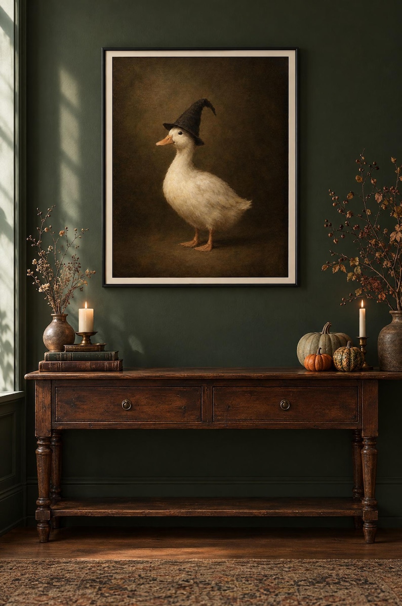 K&ouml;nnte beinhalten: Ein gerahmter Wandkunstdruck, der eine wei&szlig;e Ente mit einem schwarzen, spitzen Hexenhut zeigt. Die Ente ist im Profil vor einem dunklen, stimmungsvollen und strukturierten braunen Hintergrund dargestellt. Das Bild ist in einem schmalen schwarzen Rahmen.