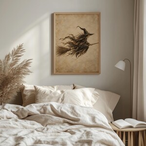 May include: A framed wall art print featuring a sepia-toned illustration of a witch wearing a pointed hat and flowing robes, riding a broomstick. The artwork has a weathered, vintage paper texture with dark brown ink lines against a beige background.