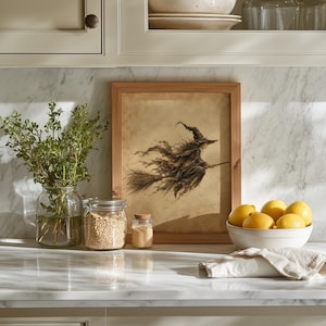 May include: A framed rectangular print featuring a dark, detailed illustration of a witch flying on a broomstick against a parchment-colored background. The artwork is displayed in a simple light-toned wooden frame, showcasing a classic artistic style.