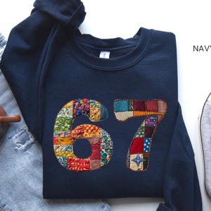 Könnte beinhalten: Marineblaues Sweatshirt mit der Zahl "67" im Patchwork-Design. Das Bild zeigt auch hellblaue Jeans, eine braune Tasse und graue Turnschuhe.