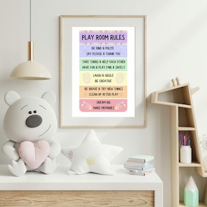 以下が含まれることがあります： 子供のプレイルームにある「PLAY ROOM RULES」というテキストが書かれた額入りのプリント。ルールには「Be Kind & Polite」、「Say Please & Thank You」、そして「Dream Big, Make Memories」が含まれています。ピンクのハートを持つ白いテディベアが白い表面に座っています。