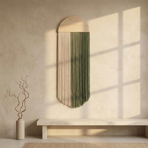 Peut inclure: Une décoration murale composée d'une pièce supérieure en bois clair en forme de demi-cercle, avec de longs fils verticaux bicolores, crème et vert olive, disposés en deux sections distinctes tombant droit depuis la base en bois.