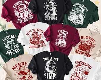 Può includere: Una collezione di felpe a tema natalizio in vari colori, ognuna con grafiche e testo umoristici. I disegni includono Babbo Natale, elfi, pupazzi di neve e altri personaggi festivi con frasi come "Check Out My Balls" e "You Ain't Gettin' Shit+".