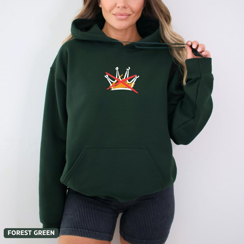 Puede incluir: Sudadera con capucha verde bosque con bolsillo delantero y capucha con cord&oacute;n. La sudadera tiene un peque&ntilde;o dise&ntilde;o de corona bordada con una l&iacute;nea roja. El texto "FOREST GREEN" est&aacute; en la parte inferior de la imagen.