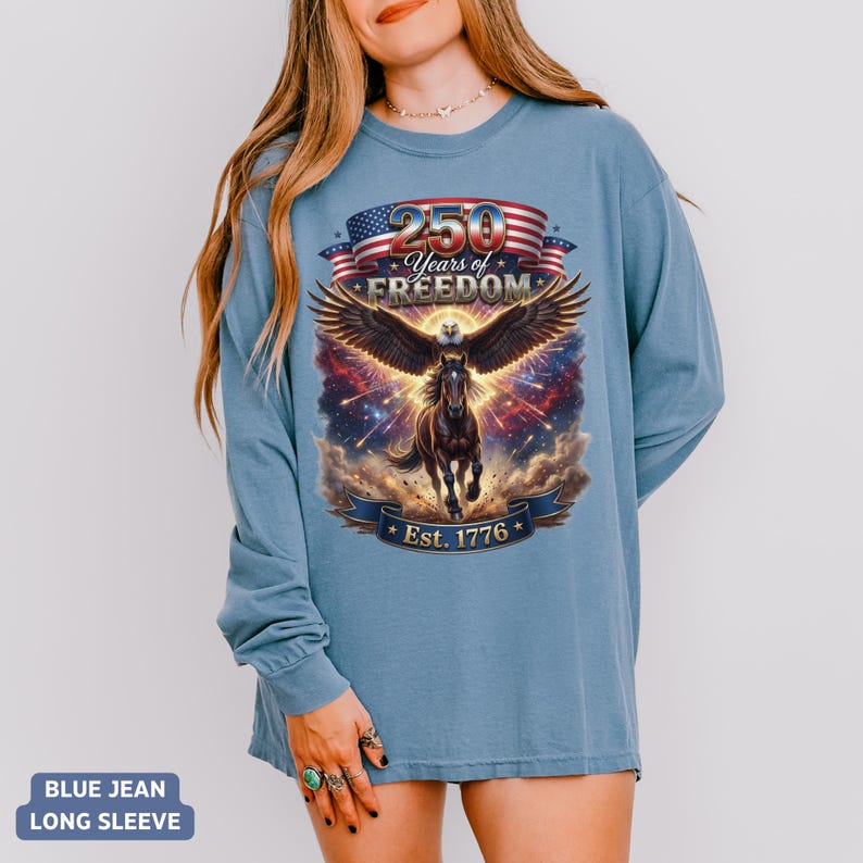 May include: A blue jean long-sleeve shirt featuring a graphic with a horse, eagle wings, and the text "250 Years of Freedom Est. 1776". The design incorporates red, white, and blue elements.