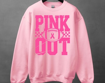 Puede incluir: Sudadera rosa claro con las palabras "PINK OUT" en letras de bloque rosa brillante desgastadas. Un balón de fútbol americano rosa con una cinta rosa en el centro. La sudadera está colgada de una percha negra.