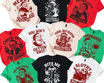 Può includere: Una collezione di magliette grafiche umoristiche in vari colori, tra cui rosso, nero, bianco e verde. Ogni maglietta presenta un design unico con testo e illustrazioni, come Babbo Natale, pupazzi di neve e omini di pan di zenzero. Le magliette hanno frasi come "Merry Kissmyass" e "Bite Me."