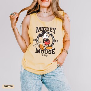 K&ouml;nnte beinhalten: Gelbes Tanktop mit Mickey Mouse-Grafik. Die Grafik enth&auml;lt die W&ouml;rter "Mickey Mouse" und "1928" mit einem Bild von Mickey Mouse. Das Tanktop hat eine einfarbige gelbe Farbe.