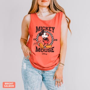 K&ouml;nnte beinhalten: Helllachsfarbenes Tanktop mit einem Mickey Mouse-Motiv. Das Design enth&auml;lt die W&ouml;rter "Mickey Mouse" und "Disney" mit den Jahren "1928" in einem kreisf&ouml;rmigen Schachbrettmuster. Das Tanktop ist &auml;rmellos.