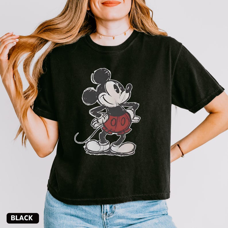 K&ouml;nnte beinhalten: Schwarzes T-Shirt mit einem verblichenen Mickey Mouse-Motiv in Schwarz, Wei&szlig; und Rot. Die Zeichentrickfigur ist in einer klassischen Pose dargestellt. Das Wort "BLACK" ist in einem wei&szlig;en Feld am unteren Rand des T-Shirts aufgedruckt.