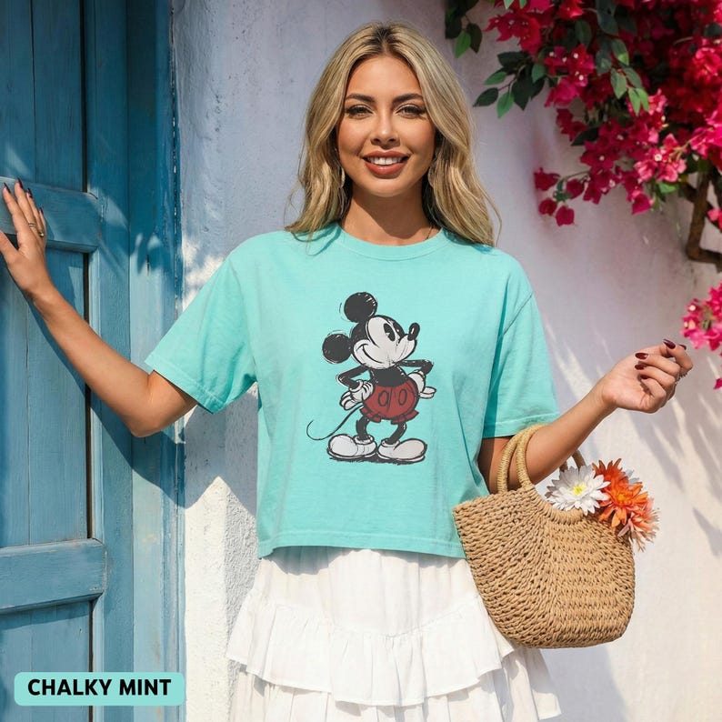 K&ouml;nnte beinhalten: Mintgr&uuml;nes T-Shirt mit einem klassischen Mickey Mouse-Motiv. Dazu ein wei&szlig;er Rock und eine geflochtene Handtasche mit Blumen. Der Text "CHALKY MINT" befindet sich am unteren Bildrand.