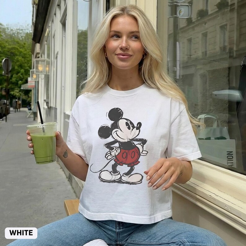 K&ouml;nnte beinhalten: Wei&szlig;es T-Shirt mit einem Vintage-Mickey-Mouse-Motiv in Schwarz, Rot und Wei&szlig;. Das Shirt hat kurze &Auml;rmel und einen Rundhalsausschnitt. Das Wort "WHITE" ist unten im Bild aufgedruckt.