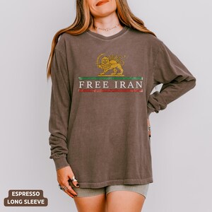Puede incluir: Camiseta de manga larga color espresso con un gr&aacute;fico que dice "FREE IRAN". El gr&aacute;fico presenta un le&oacute;n dorado con un sol, encima de una franja verde y roja. La camiseta es de corte holgado.
