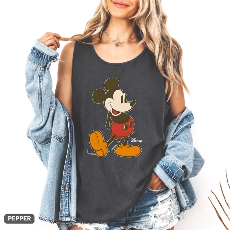 Puede incluir: Una camiseta de tirantes gris oscuro con un estampado gr&aacute;fico de Mickey Mouse con pantalones cortos rojos y zapatos amarillos. El personaje aparece en una pose cl&aacute;sica con la palabra Disney en blanco. La palabra Pepper es visible en la imagen.