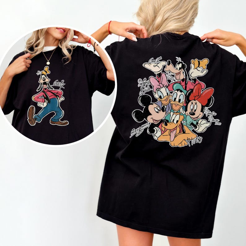 Pode incluir: Camiseta preta com uma imagem de desenho animado do Pateta na frente e um grupo de personagens da Disney nas costas. O gr&aacute;fico do Pateta mostra-o com uma camisa vermelha, cal&ccedil;as azuis e um chap&eacute;u amarelo. As costas apresentam Mickey, Minnie, Donald, Margarida, Pluto e Pateta.