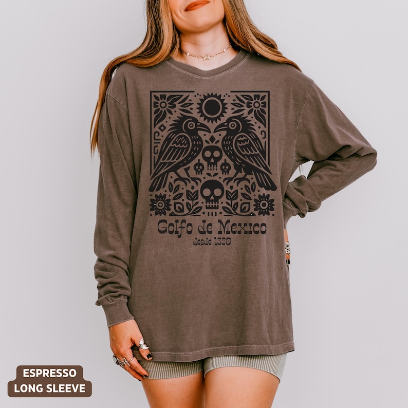 Puede incluir: Camiseta de manga larga color espresso con un dise&ntilde;o gr&aacute;fico negro. El dise&ntilde;o incluye dos cuervos, calaveras, flores y el texto "Golfo de Mexico desde 1500". La camiseta tiene un corte holgado.