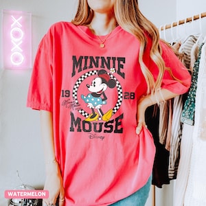 K&ouml;nnte beinhalten: Ein pinkfarbenes T-Shirt mit einem Minnie Mouse-Motiv. Das Design enth&auml;lt den Text "MINNIE MOUSE" in fetter Schrift, mit dem Disney-Logo unten. Das T-Shirt hat eine Vintage-&Auml;sthetik und ist einfarbig.