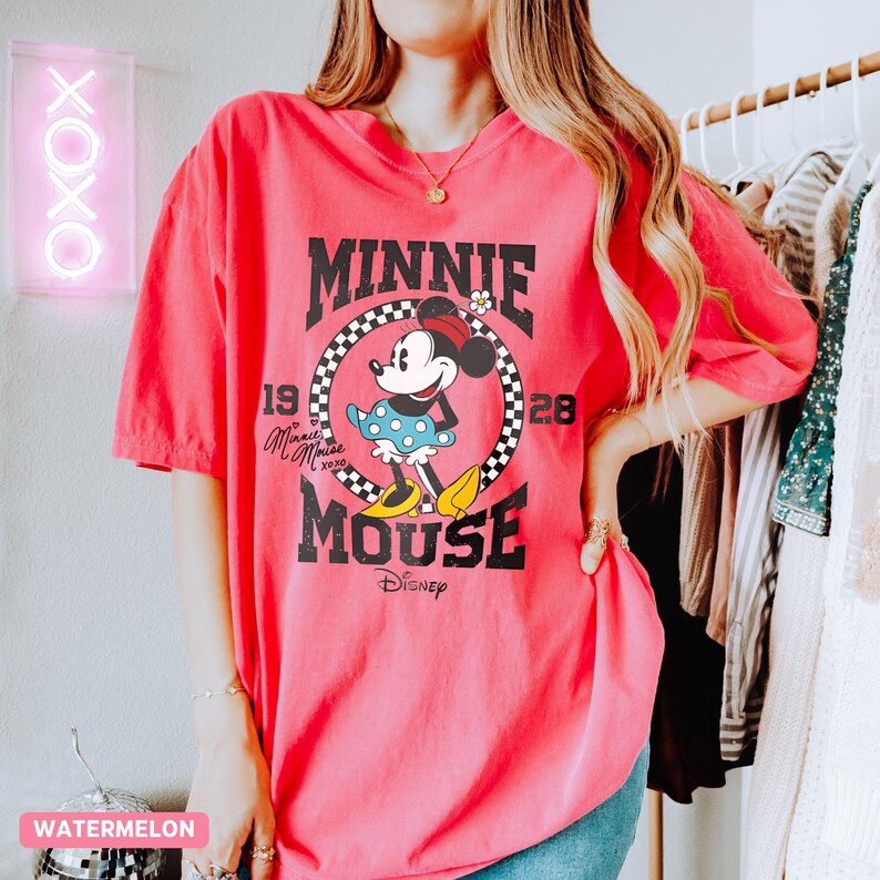 K&ouml;nnte beinhalten: Ein pinkfarbenes T-Shirt mit einem Minnie Mouse-Motiv. Das Design enth&auml;lt den Text "MINNIE MOUSE" in fetter Schrift, mit dem Disney-Logo unten. Das T-Shirt hat eine Vintage-&Auml;sthetik und ist einfarbig.