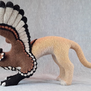 Pu&ograve; includere: Una scultura in feltro marrone e beige di un grifone con le ali spiegate. Il grifone ha un corpo da leone con una testa e ali da uccello. La scultura &egrave; dettagliata con accenti neri e bianchi.