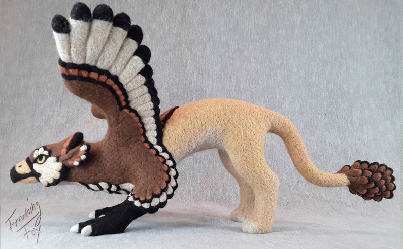 Pu&ograve; includere: Una scultura in feltro marrone e beige di un grifone con le ali spiegate. Il grifone ha un corpo da leone con una testa e ali da uccello. La scultura &egrave; dettagliata con accenti neri e bianchi.