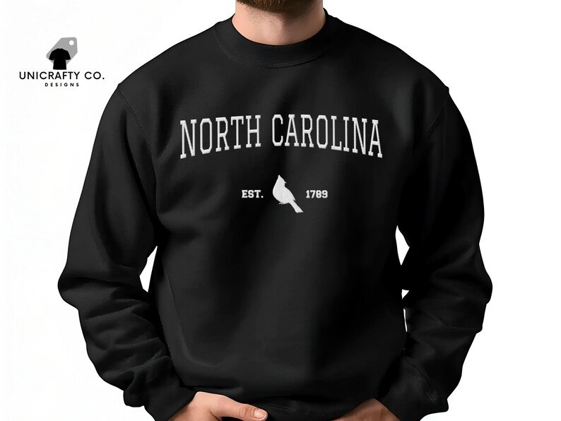 May include: Black sweatshirt featuring the text "NORTH CAROLINA" in white, arched across the chest. Below the text is a white cardinal and the text "EST. 1789". The sweatshirt is a crew neck style.
