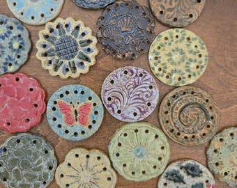 May include: A collection of circular ceramic discs featuring various embossed patterns, including a butterfly, floral motifs, shells, and swirls. Each disc has a series of small holes around the perimeter and centre, finished in diverse glazes.