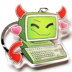 Pode incluir: Um porta-chaves de acrílico transparente com um computador de desenho animado com um rosto sorridente, chifres de diabo vermelhos e uma seta vermelha. Dois corações rosa também estão incluídos no design. O computador tem um ecrã e um teclado verdes.