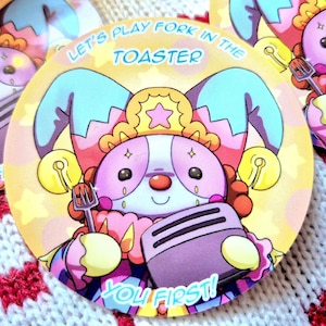 Könnte beinhalten: Ein runder Aufkleber mit einem Cartoon-Jester, der einen Toaster und eine Gabel hält. Der Aufkleber hat einen gelben Hintergrund mit Sternen und dem Text "Let's play fork in the toaster. You first!"