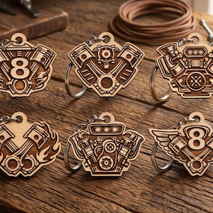 May include: Six wooden keychains with engine designs. The keychains are laser-cut with intricate details, including pistons, gears, and the number 8. Each keychain has a silver-colored ring for attaching keys. The wood has a natural, light brown color.