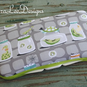 May include: A rectangular eyeglasses case with a gray background featuring a repeating pattern of jars with insects and reptiles. The case has a green trim and the text "Laura Lee Designs" in the upper left corner.