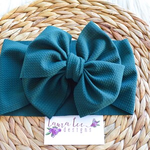Peut inclure: Un grand bandeau à nœud vert foncé. Le nœud est fait d'un tissu doux et texturé. Le bandeau est sur une surface tissée.