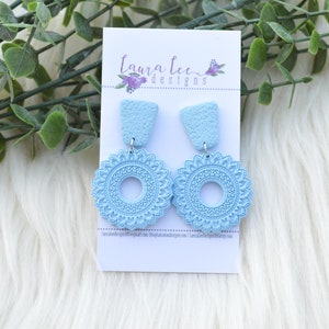 Puede incluir: Un par de pendientes colgantes de color azul claro con un diseño de mandala. Los pendientes están en una tarjeta blanca con el texto "laura lee designs".