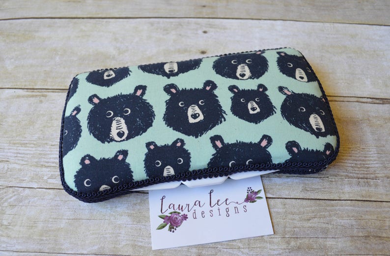 May include: Rectangular fabric pouch with a repeating pattern of black bear faces on a light teal background. The pouch is trimmed with a dark navy blue border and a decorative black trim. A small white card with the text "Laura Lee Designs" is in the foreground.